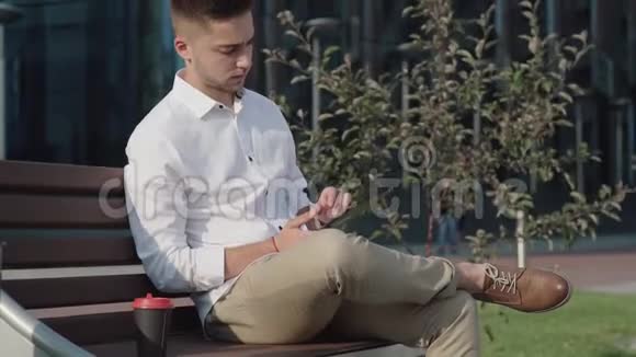 年轻的时尚男士坐在长凳上腿朝腿上一甩视频的预览图