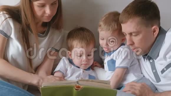 一家人的爸爸妈妈和两个双胞胎兄弟躺在床上看书家庭阅读时间视频的预览图