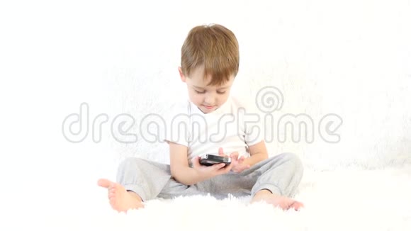一个孩子坐在白色沙发上玩智能手机玩得很开心视频的预览图