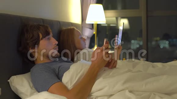 男人和女人躺在床上每个人都有智能手机和平板电脑女人关掉灯男人睡觉视频的预览图