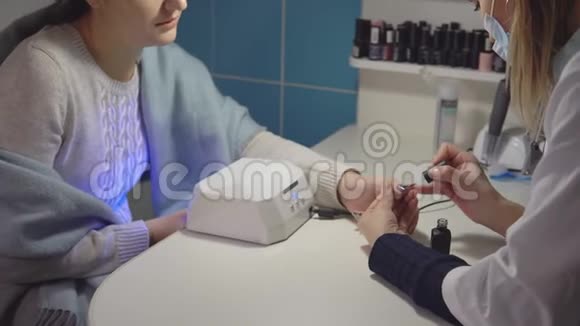 指甲艺术家在美容院给一个年轻女人做指甲背景上钉子的瓶子视频的预览图