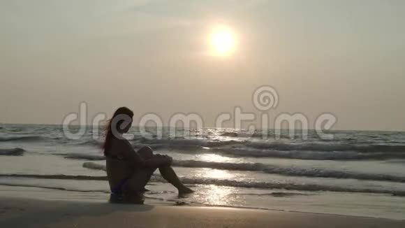 那个女孩正坐在日落时在海滩上做梦4K视频的预览图