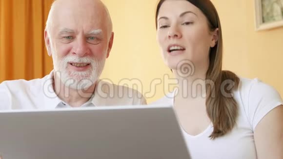 老人和女儿在家里通过笔记本电脑上的messenger应用程序进行视频聊天微笑挥手视频的预览图