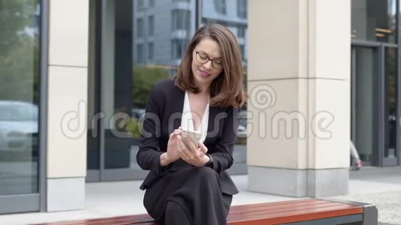 用智能手机坐在长凳上的女商人视频的预览图