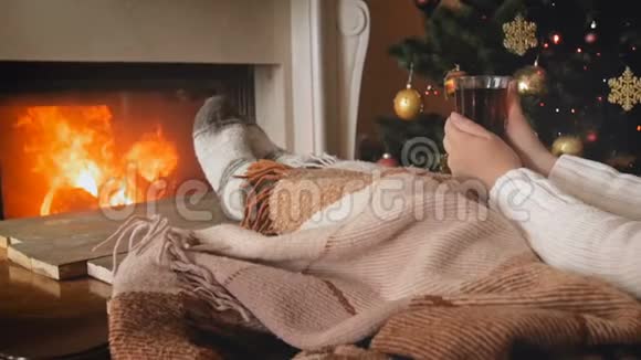 在圣诞节前夕躺在沙发上燃烧着的壁炉旁喝着茶的女人的视频视频的预览图