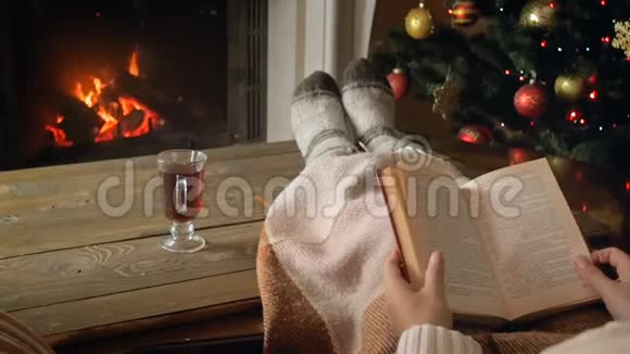 圣诞节晚上一位年轻女子躺在格子布下燃烧着的壁炉和喝茶的慢镜头视频的预览图