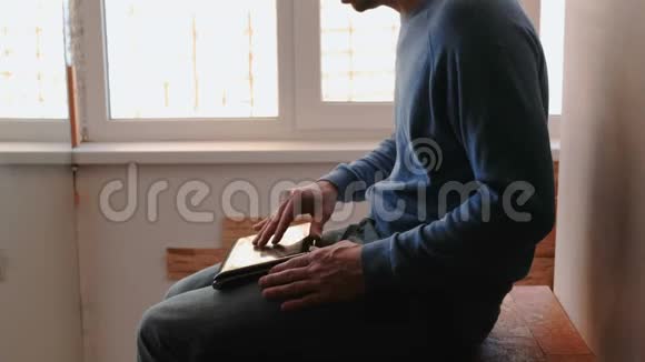 在笔记本电脑上工作无法辨认的年轻人打开笔记本电脑在靠近窗户的阳台上打字视频的预览图