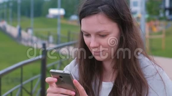 年轻的黑发女人在城里散步的长廊上聊天在手机上输入一条信息视频的预览图