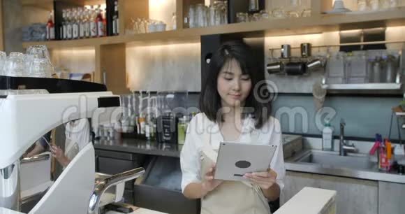 年轻的亚洲咖啡师在咖啡店休息时使用平板电脑视频的预览图