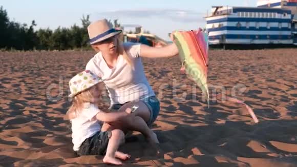 戴着帽子的金发美女妈妈和女儿在海滩上放风筝视频的预览图