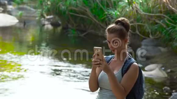 女游客带着背包在手机上拍照在丛林森林里徒步旅行年轻女性使用智能手机视频的预览图