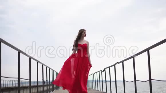 一个年轻而浪漫的女人穿着一件红色的长裙站在码头上视频的预览图