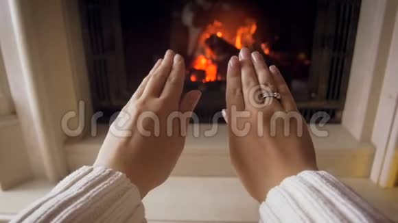 年轻女子用冰冷的双手在家里的壁炉里摩擦和伸展着燃烧的火的慢镜头视频的预览图