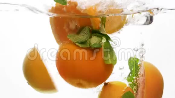 特写4k片多汁切好的橙子和柠檬薄荷叶在冷水中倒在白色的果岭上视频的预览图