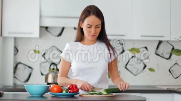 快乐的年轻家庭主妇在舒适的厨房里切鲜黄瓜视频的预览图