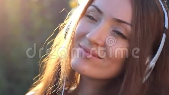 戴着耳机的女人在日落时听音乐在一个美丽的特写女孩的户外肖像上有阳光视频的预览图