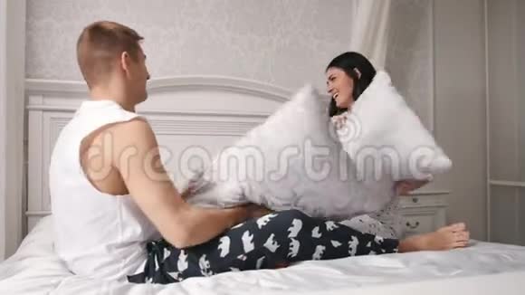 快乐快乐的恋人在床上打枕头亲吻男人和女孩穿着睡衣视频的预览图