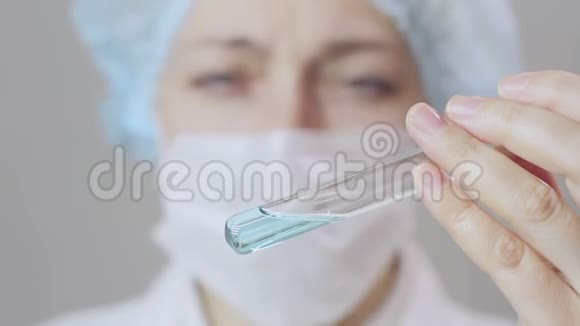 一名身穿白衣的女医生和防护手套将蓝色液体倒入试管中视频的预览图