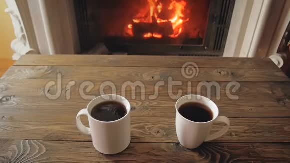 近景慢镜头两个杯子热茶放在木桌旁燃烧的壁炉视频的预览图