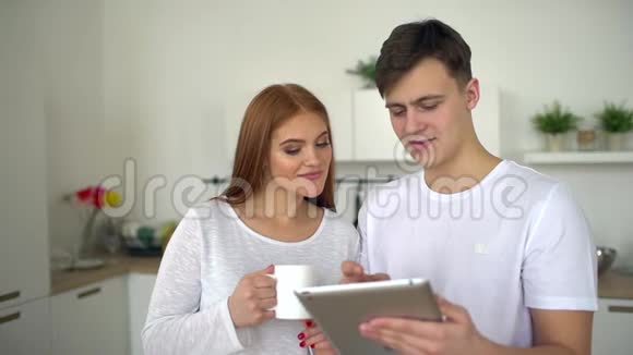 合上可爱快乐的小情侣抱着微笑看着平板电脑屏幕在家里视频的预览图