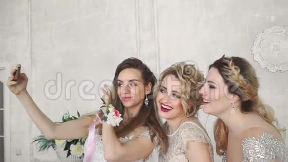 三个金发女孩在白色墙壁背景上做自拍的慢动作视频的预览图