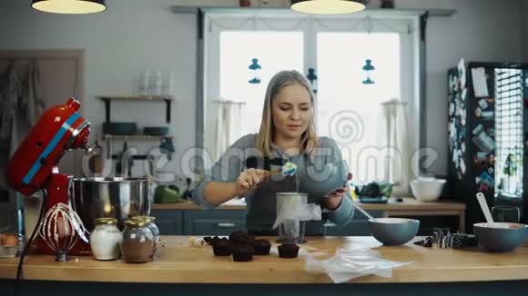 年轻的金发女人在厨房做饭美丽的女性准备奶油装饰纸杯蛋糕做她的爱好视频的预览图