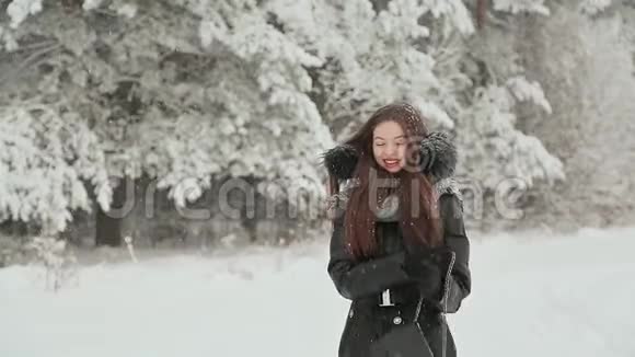 一个穿着长头发的冬衣的年轻女孩在降雪下沿着白雪覆盖的森林散步视频的预览图