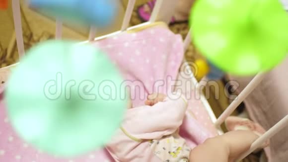 婴儿躺在有玩具的婴儿床上并在他身边翻身动作缓慢视频的预览图