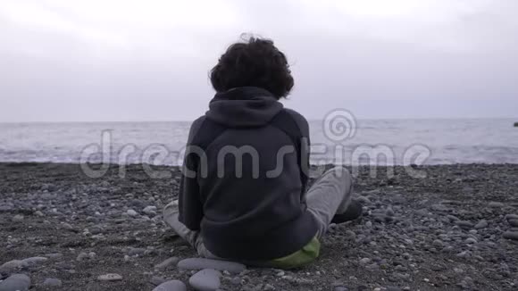 一个孤独的男孩坐在海滩上4k慢动作视频的预览图