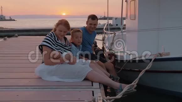 日落时分父母和大儿子坐在码头上视频的预览图