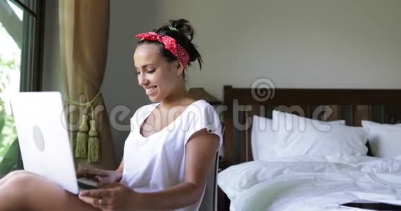 年轻女性使用笔记本电脑美丽的女孩在线聊天在卧室的早晨在大窗户上视频的预览图