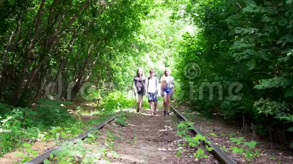 阳光明媚的一天年轻的朋友在森林废弃的铁路上散步视频的预览图