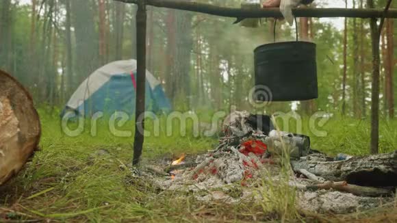 营地火灾中的大锅男人用杯子舀东西视频的预览图