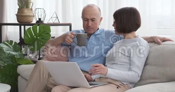 年长夫妇在沙发上喝咖啡使用笔记本电脑视频的预览图