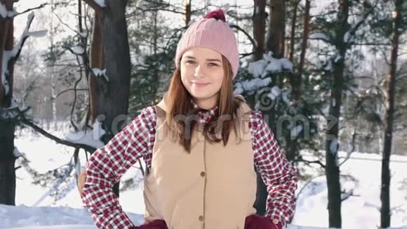 冬天的森林阳光下一个穿着红色衬衫和帽子的微笑可爱女孩的肖像视频的预览图