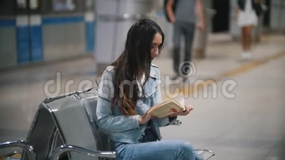 坐在地铁长凳上拿着书的女孩慢动作视频的预览图