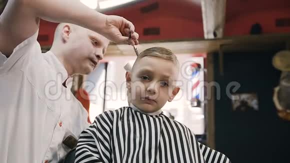 一个可爱的男孩坐在理发店的椅子上看着镜头用手显示一切都很好他视频的预览图