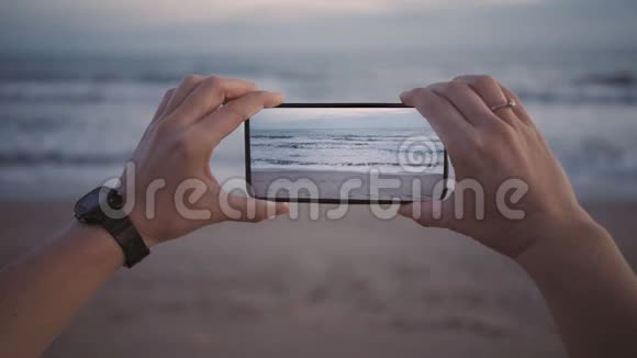 在黄昏时分用宽屏的新智能手机拍摄沙滩海浪视频的预览图