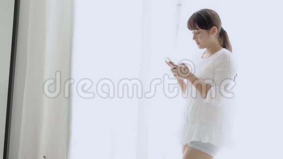 美丽的肖像年轻的亚洲女人微笑着站着看着智能手机阅读社交网络视频的预览图