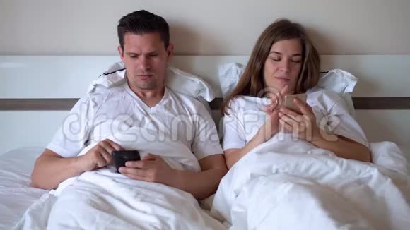夫妻俩躺在床上看智能手机视频的预览图