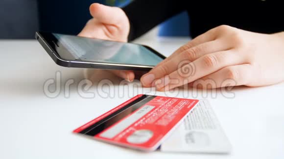 年轻女性在智能手机上浏览网上商店的特写镜头两张信用卡躺在她旁边的桌子上视频的预览图
