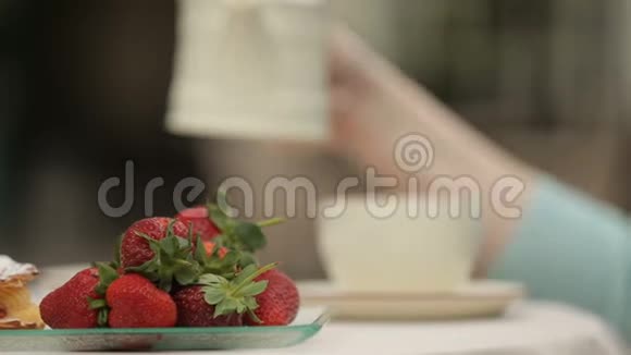女人在杯子里倒茶在户外咖啡馆放松在桌子上放草莓盘子视频的预览图