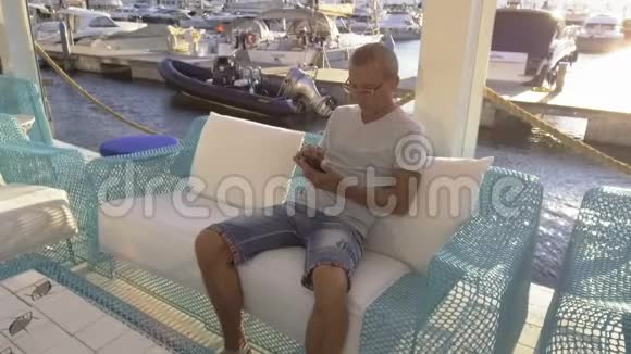 一个男人坐在码头的咖啡馆里用他的电话视频的预览图