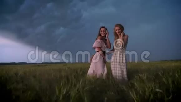 两个穿着裙子的年轻迷人的女孩在夏天的雨天在田野里迎风招展自由观念调情观念视频的预览图