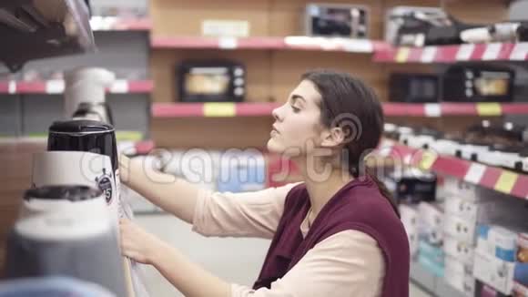 年轻女性消费者在电器商店里选择新的电热水壶并在橱窗里连续比较不同型号视频的预览图
