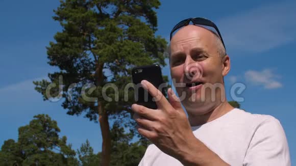 夏天公园里微笑的男人用手机通过视频聊天打电话视频的预览图