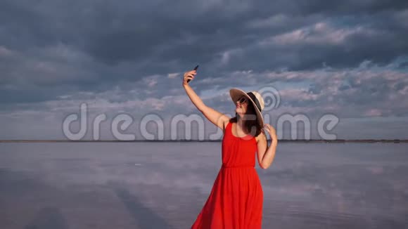 年轻的女游客在一个美丽的不寻常的地方自拍穿着红色裙子帽子和太阳镜的女孩在粉红色的湖上视频的预览图