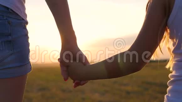 母亲和女儿在日落时在草地上散步和牵手妈妈的双手紧紧地抓住视频的预览图