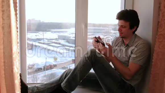 男人在手机里玩游戏坐在窗台上笑视频的预览图
