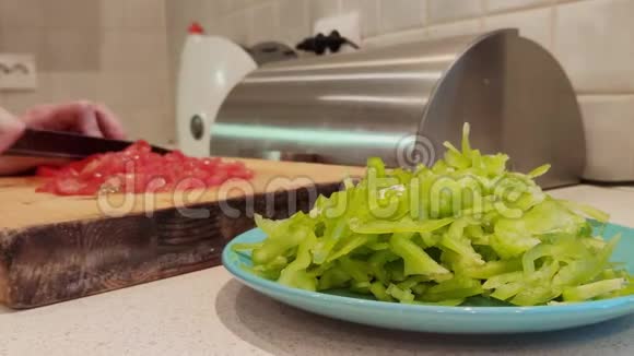 一盘切碎的绿色辣椒的特写以女性手切番茄为背景视频的预览图